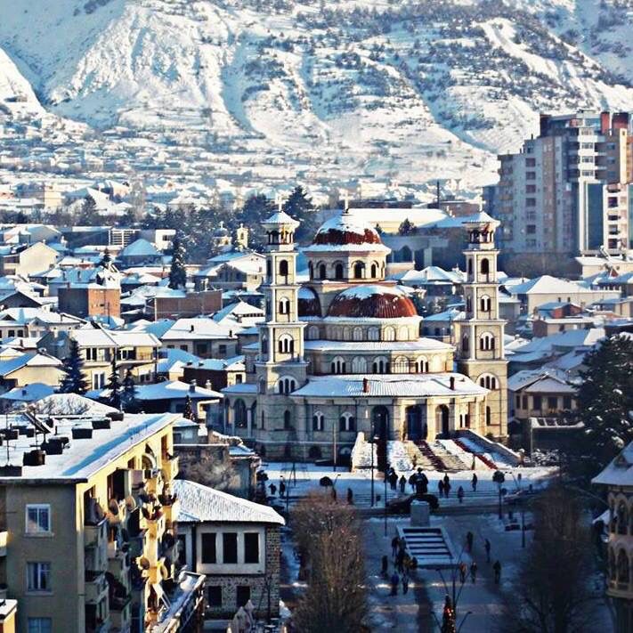 the city is covered in snow with mountains in the backgrouds and buildings on either side