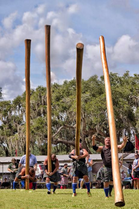 men in kilts playing with large wooden poles on grass field next to trees and people watching