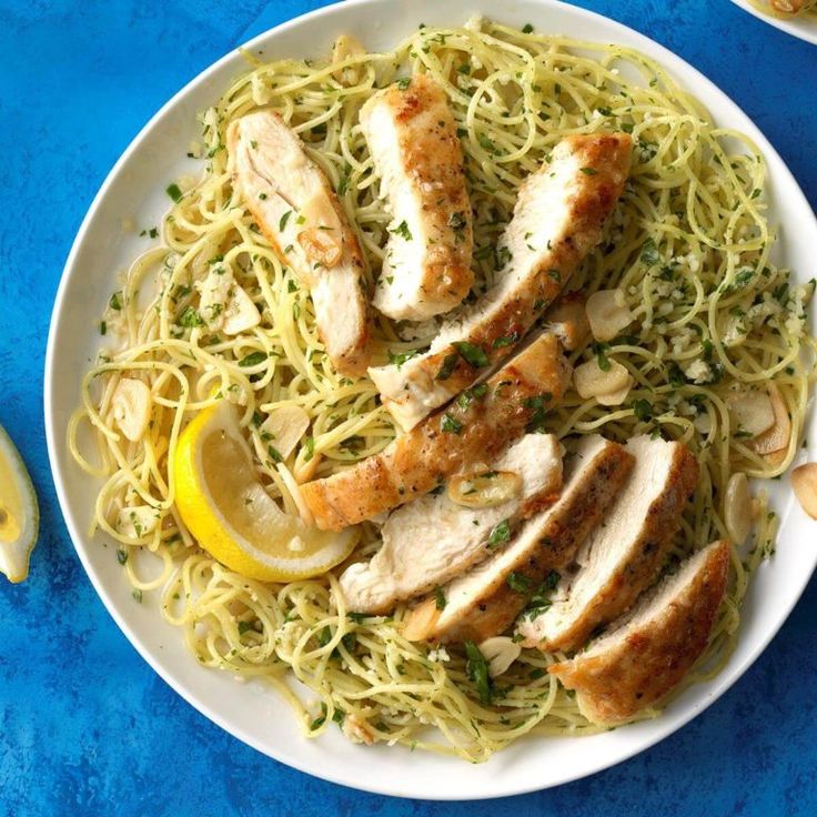 a white plate topped with chicken and pasta next to lemon wedges on a blue table