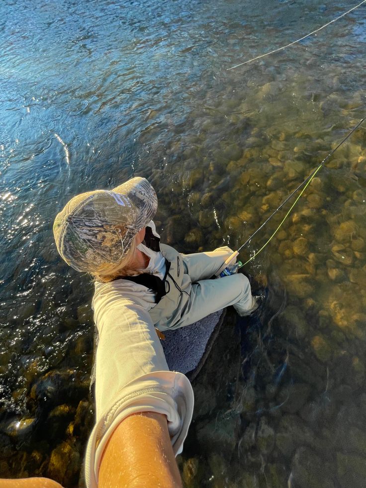 a person standing in the water holding onto a fishing line while wearing a white hat