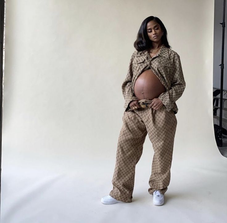 a pregnant woman standing in front of a white backdrop with her hands on her hips