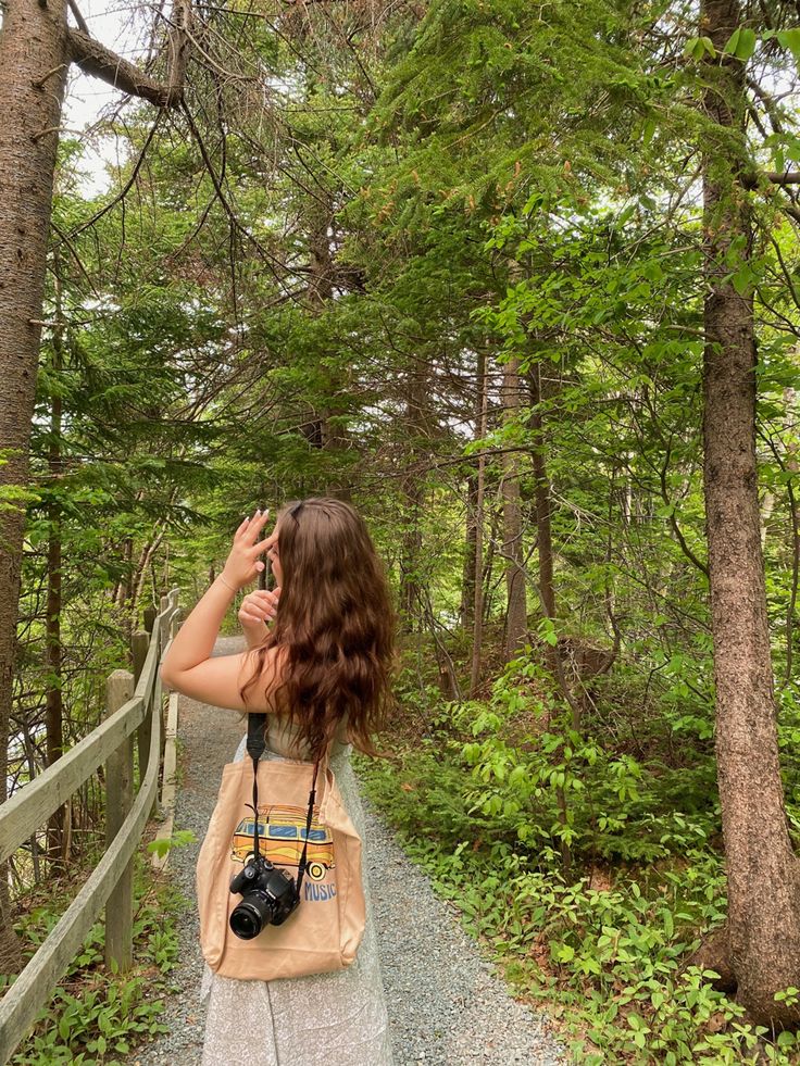 a woman standing on a path in the woods taking pictures with her cell phone and camera