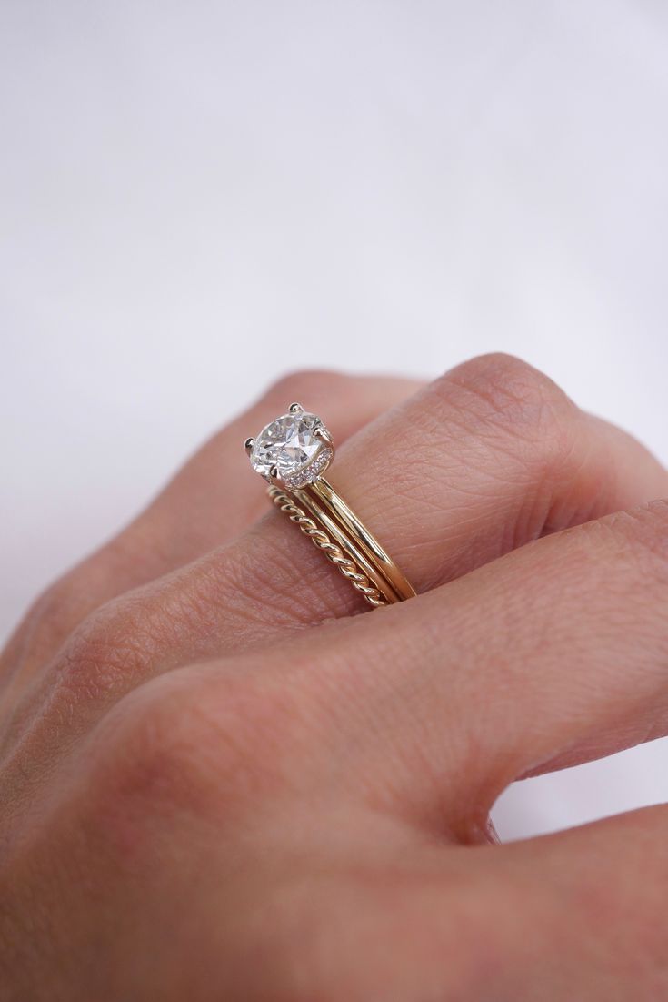 a woman's hand holding a diamond ring on top of her finger, with the engagement band in yellow gold