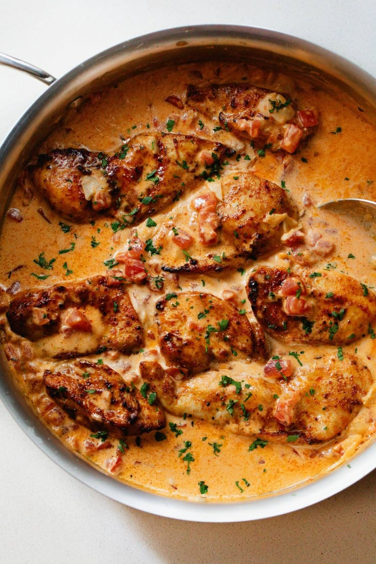 a pan filled with meat and sauce on top of a white table next to a spoon