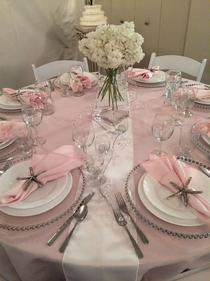 the table is set with silverware and pink napkins, white flowers in a vase