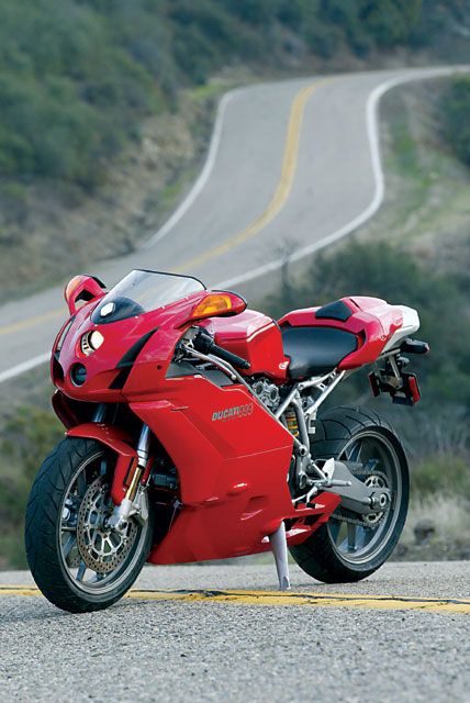 a red motorcycle is parked on the side of the road next to a winding hill