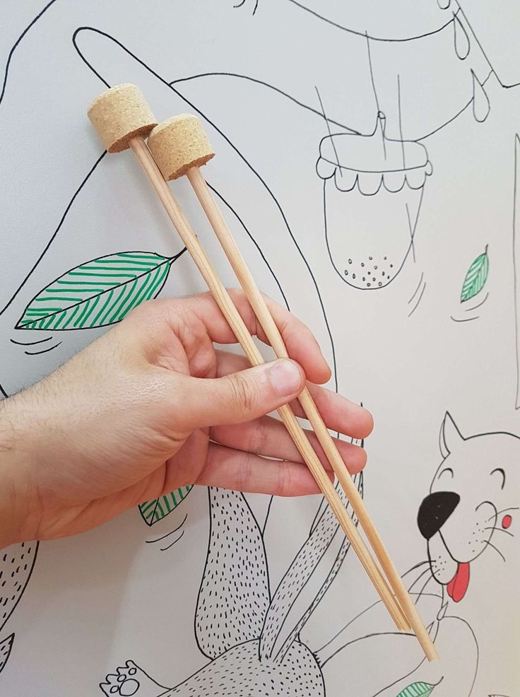 a person holding two chopsticks in front of a wall with cartoon drawings on it