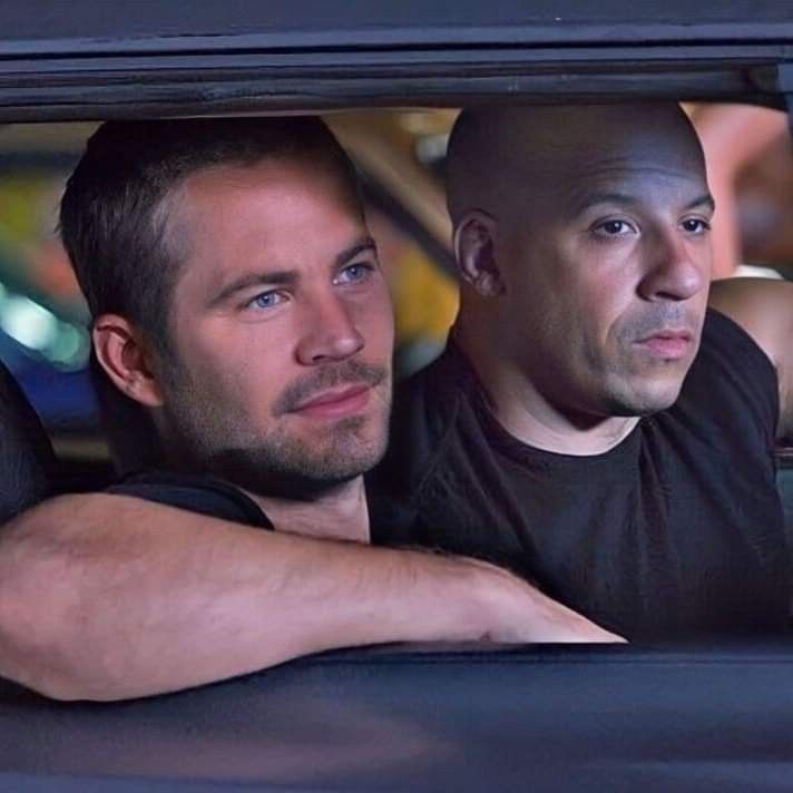 two men sitting in the drivers seat of a car looking out the window at something