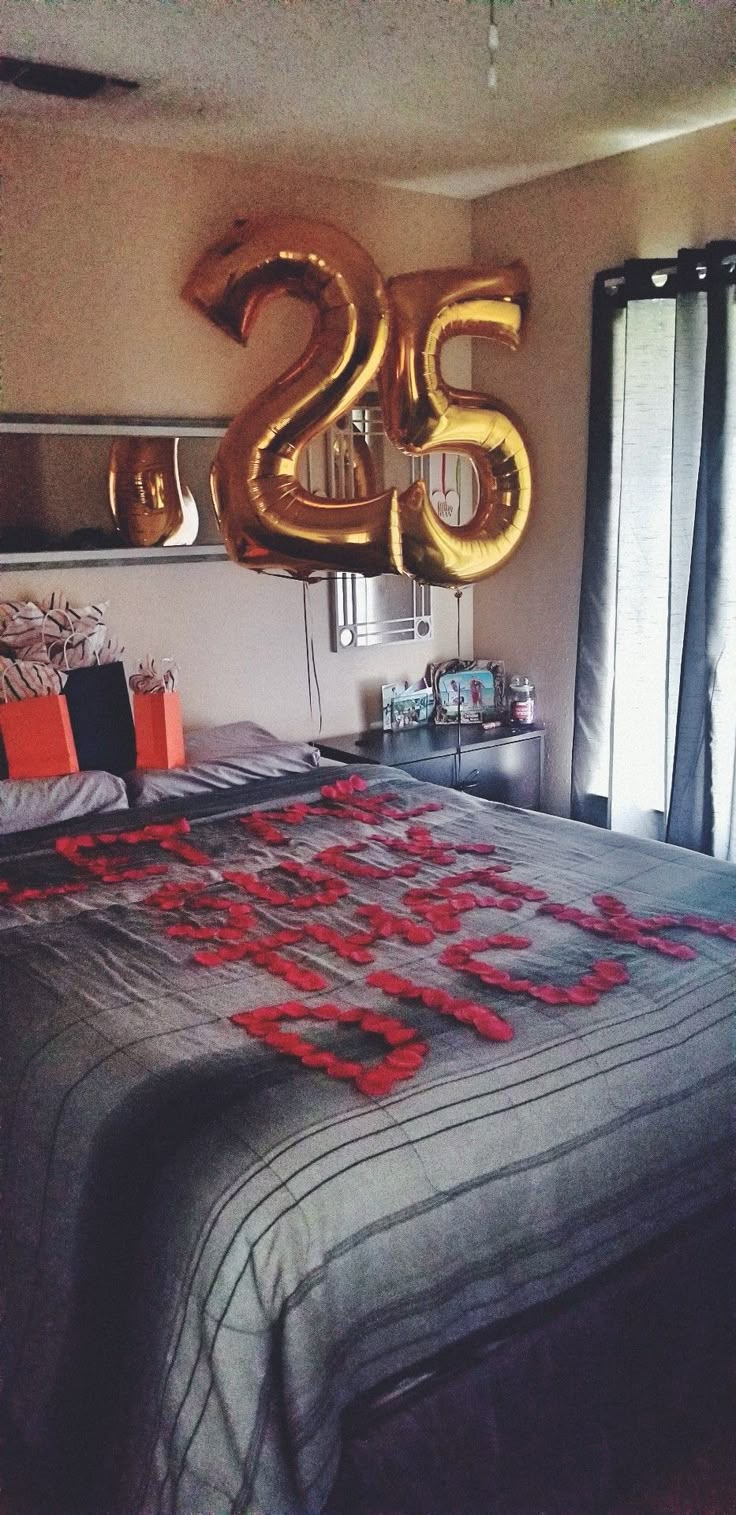 the bed is decorated with red flowers and gold foil balloons that spell out the number twenty five