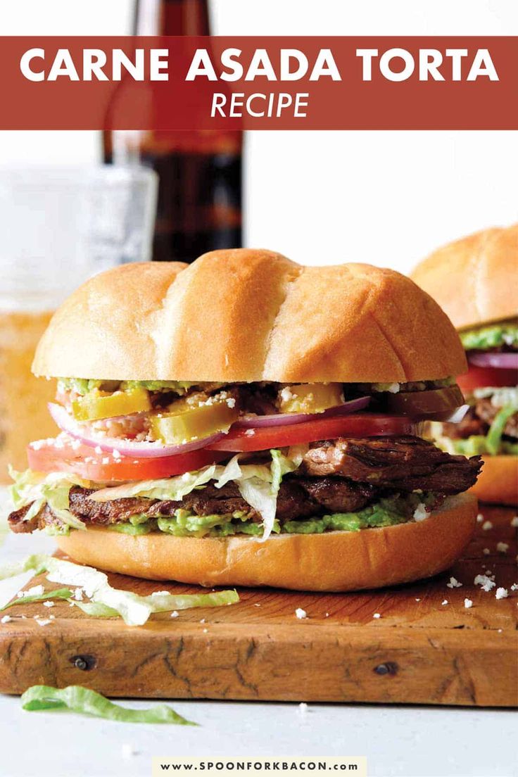 two hamburgers with lettuce, tomato and other toppings on a cutting board