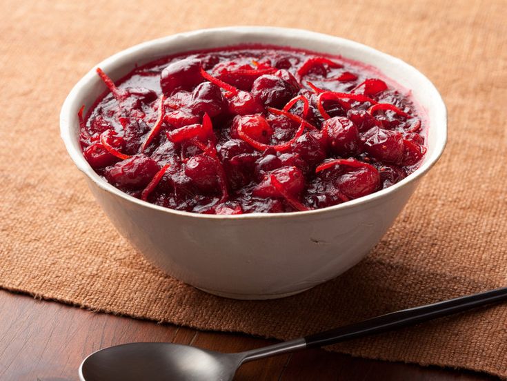 a white bowl filled with cranberry sauce next to a black spoon on top of a table