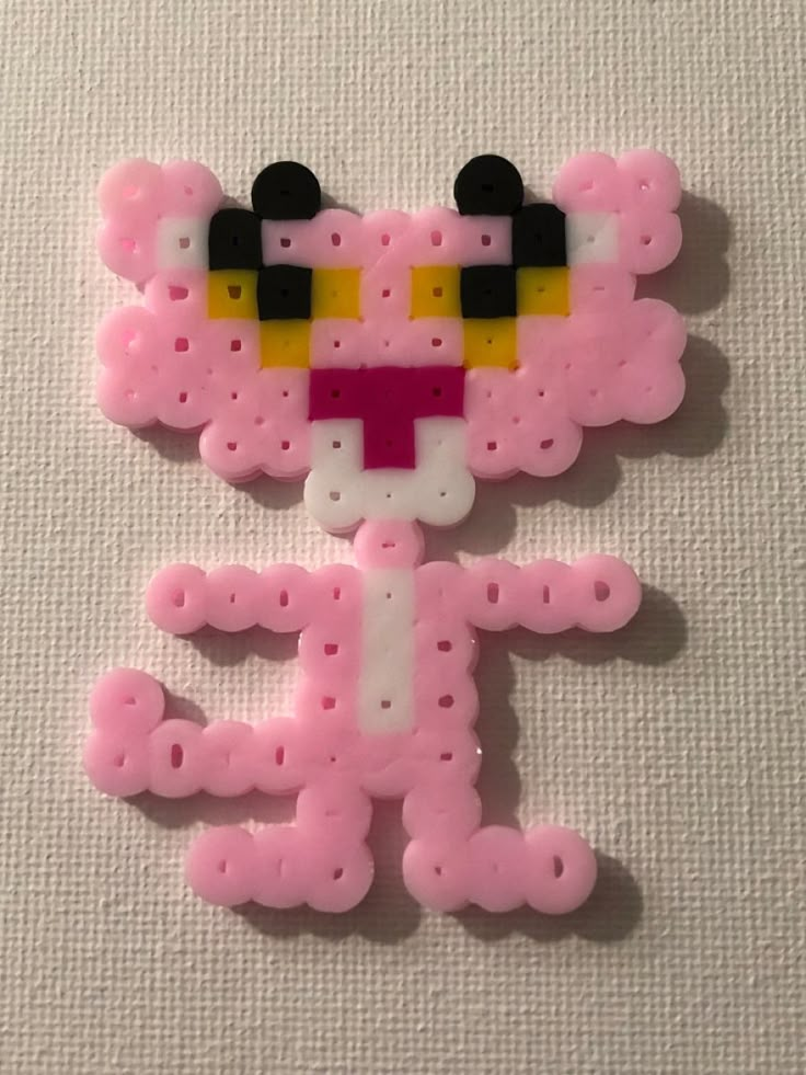 a pink teddy bear with yellow eyes and black ears on it's face is made out of plastic beads