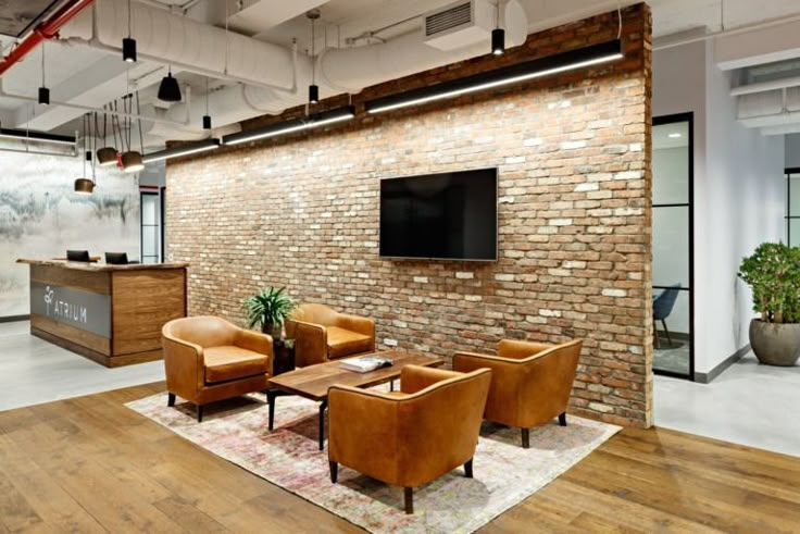 an office with brick walls and leather chairs in front of a flat screen tv on the wall