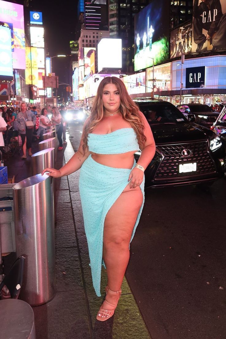 A woman stands confidently in Times Square at night, wearing a light blue two-piece outfit with a thigh-high slit. Bright billboards and city lights illuminate the bustling street behind her. Last Friday Night, Dark Beauty Photography, Oh Polly, Last Friday, Curvy Women Jeans, Lifestyle Ideas, Curvy Plus Size, Runway Show, Dark Beauty