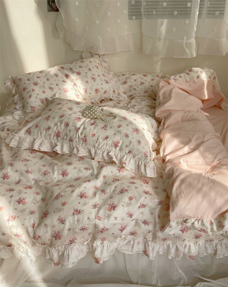 an unmade bed with pink comforters and pillows on top of it in front of a window