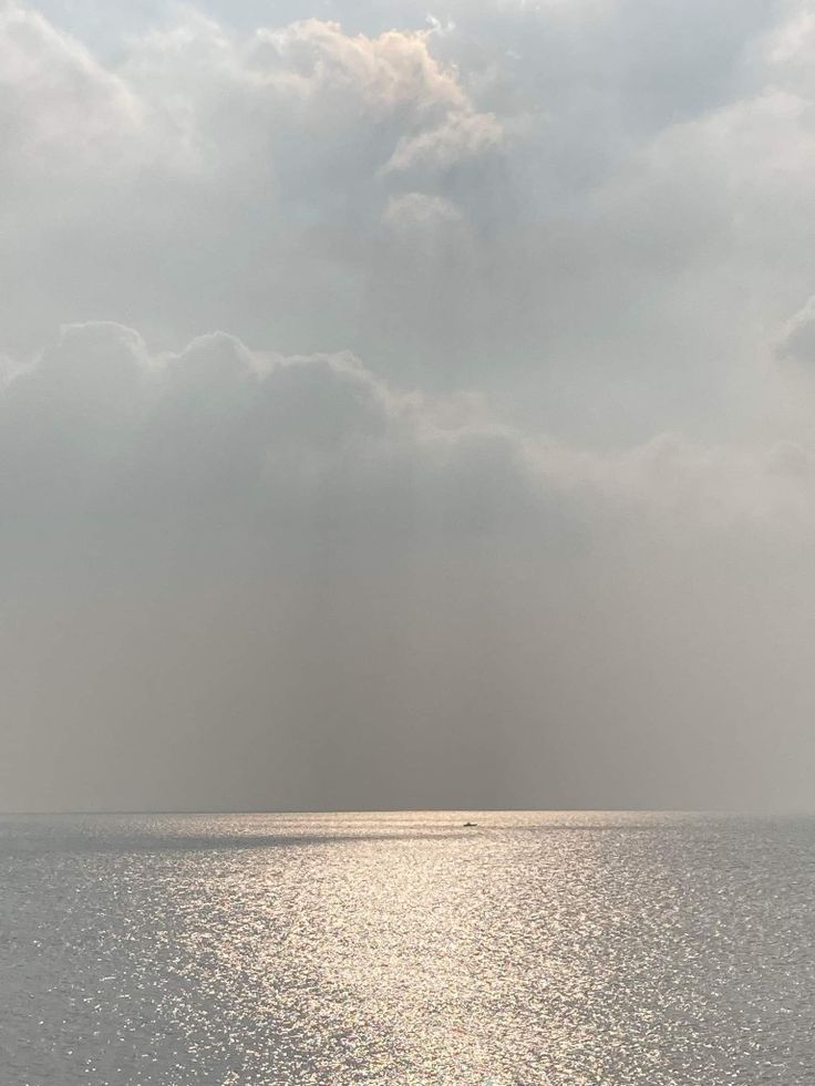 a lone boat floating in the ocean on a cloudy day