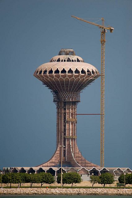 a very tall tower with a crane on it's side next to the water