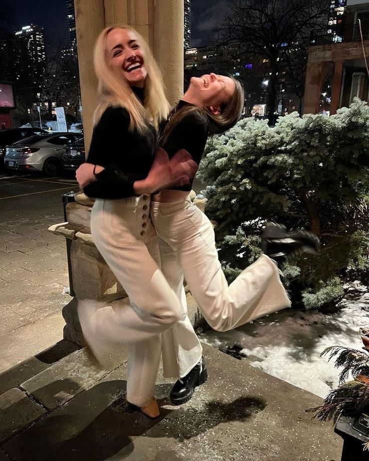 two women are posing for the camera in front of a building at night with snow on the ground