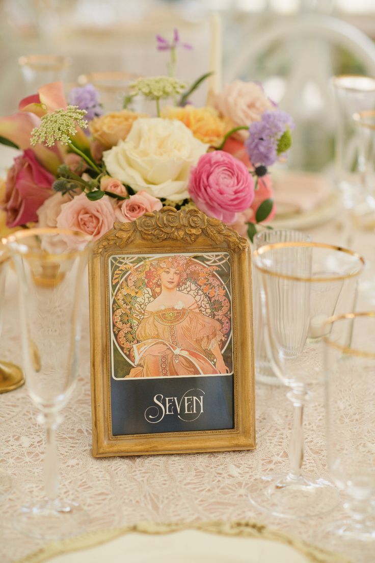 there is a table set with flowers and wine glasses on it, including an ornate framed photo