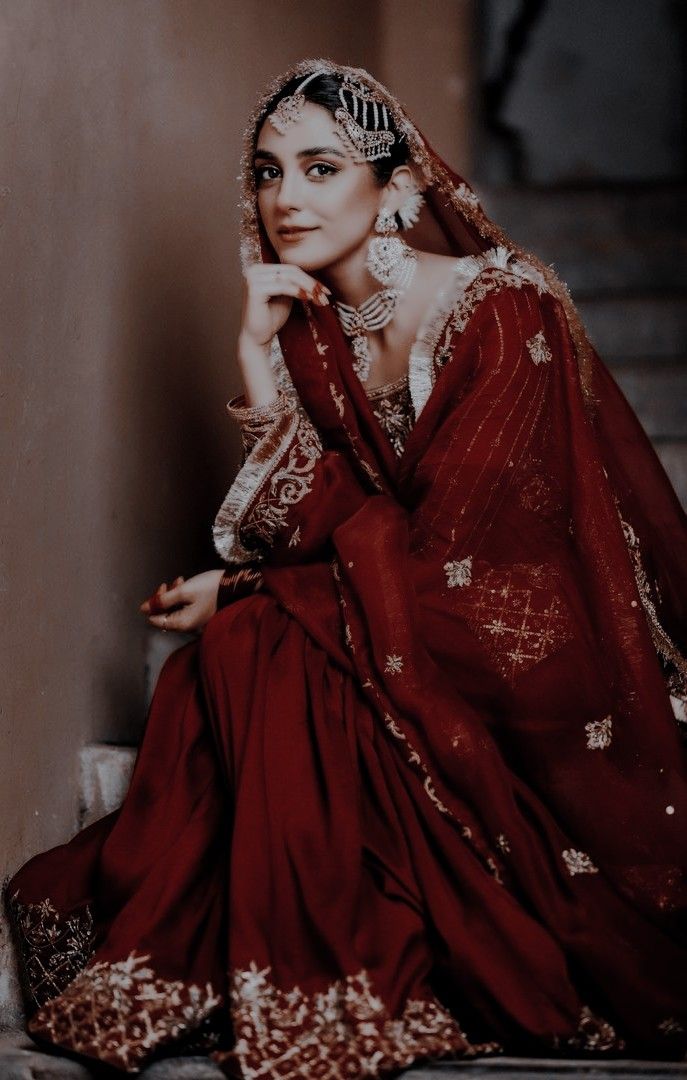 an old photo of a woman wearing a red sari and headpiece sitting on steps