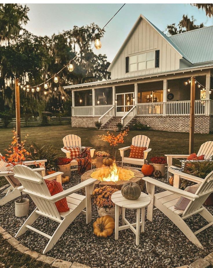 a fire pit surrounded by chairs and pumpkins in front of a house with lights on