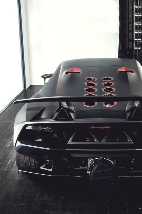 the rear end of a black sports car parked in a room with wood flooring