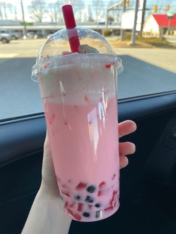 a person holding up a pink drink in their hand with strawberries and blueberries on it