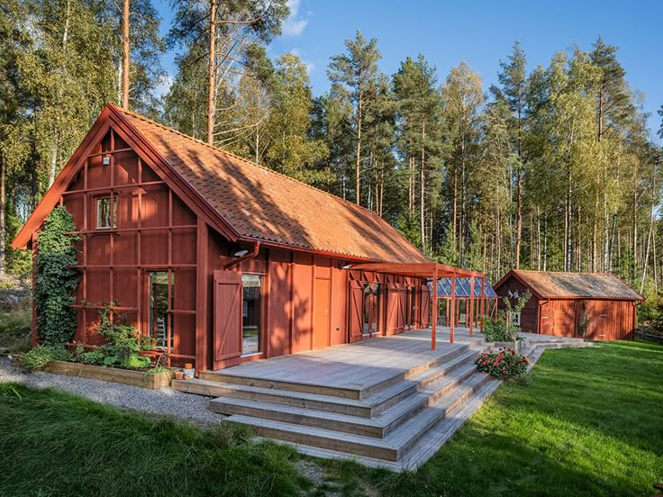 a red house sitting in the middle of a lush green field next to tall trees