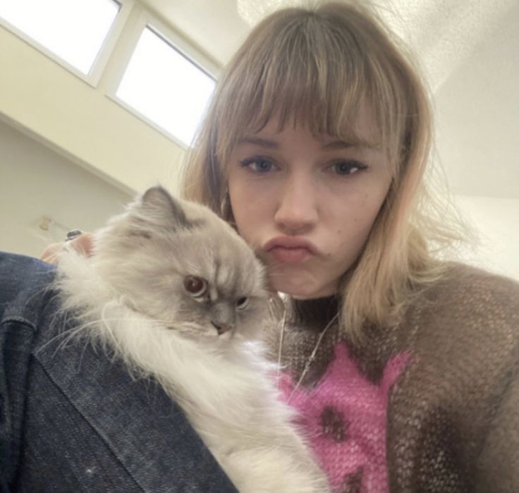 a woman holding a cat in her arms and looking at the camera with an intense look on her face