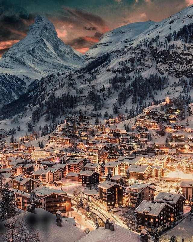 a town in the mountains covered in snow at night with lit up buildings and lights