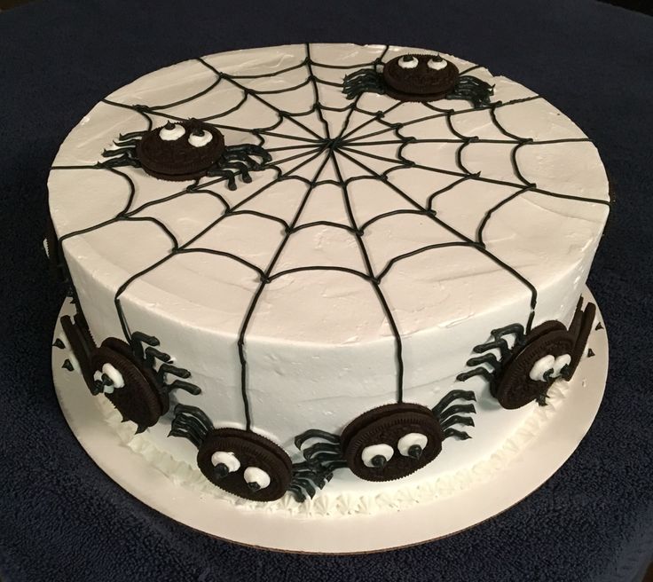 a spider web cake is decorated with white frosting and black icing on a blue tablecloth