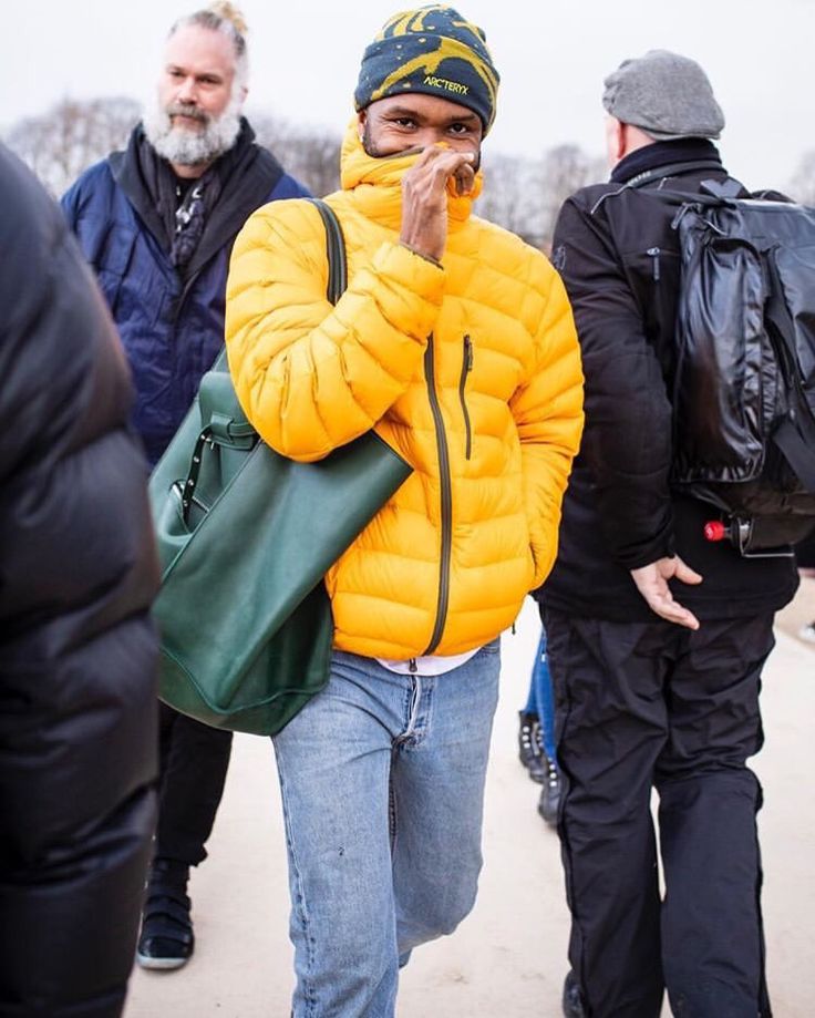 a man in a yellow jacket is talking on his cell phone while others are walking behind him