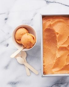 two scoops of ice cream in a metal pan next to a spoon on a marble surface