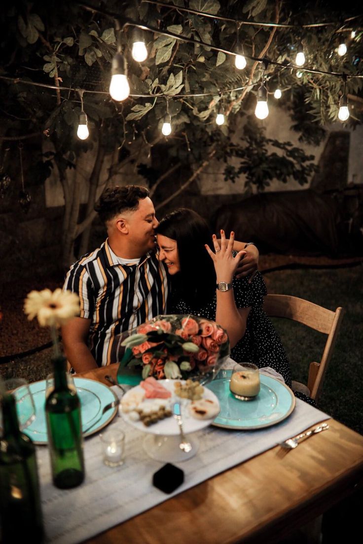 a man and woman sitting at a table with food in front of them, surrounded by lights