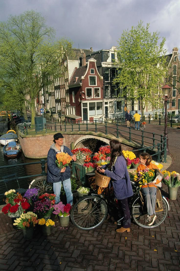 three people standing next to bicycles with flowers on the back in front of some buildings