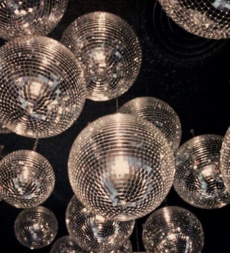 many disco balls are hanging from the ceiling in front of a black background with white lights