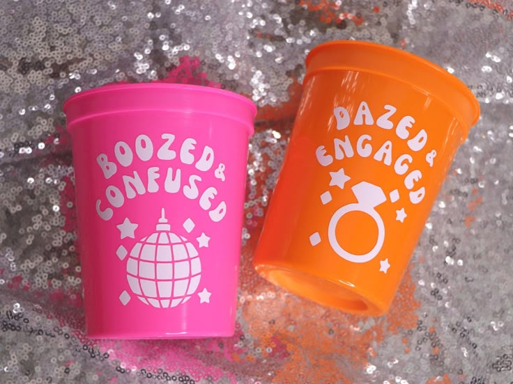 two plastic cups sitting next to each other on top of a glitter covered surface,