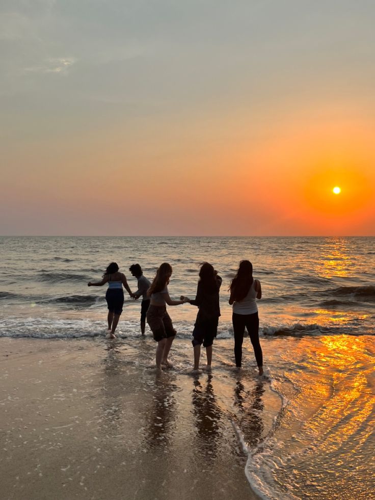 four girls standing on the beach at sunset with their arms around each other as the sun sets