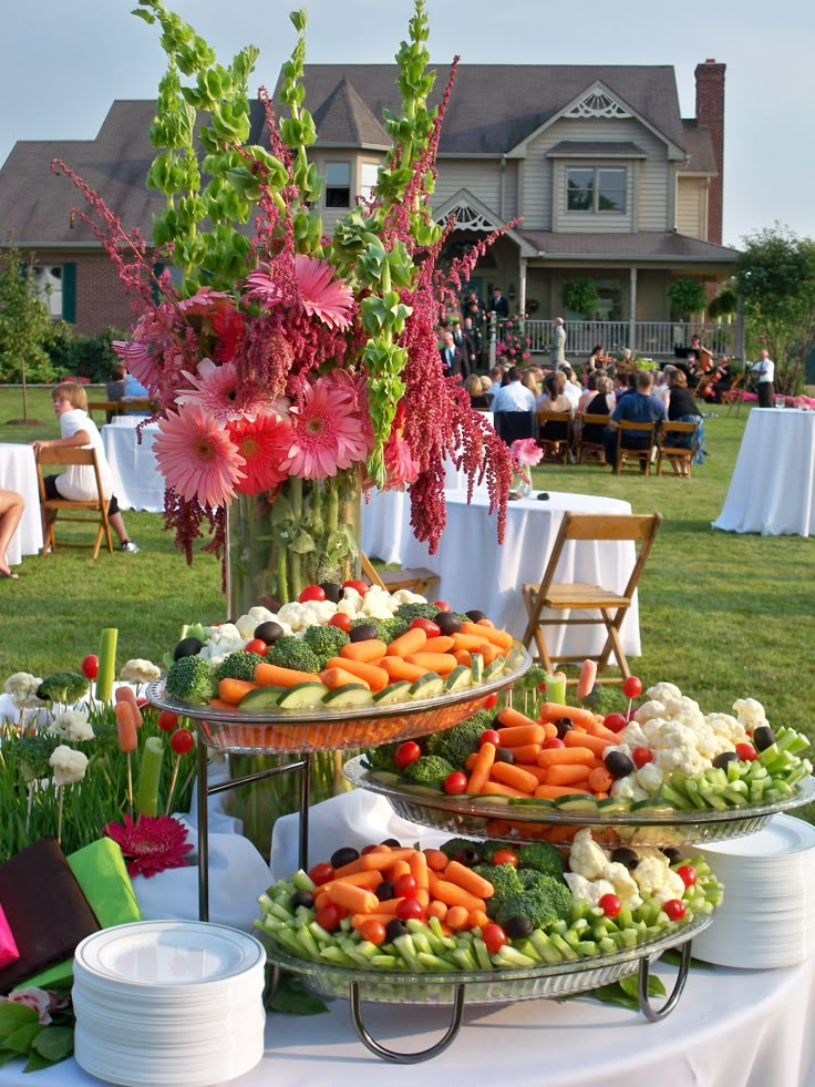 an assortment of fresh vegetables on display in front of a large house with people sitting at tables