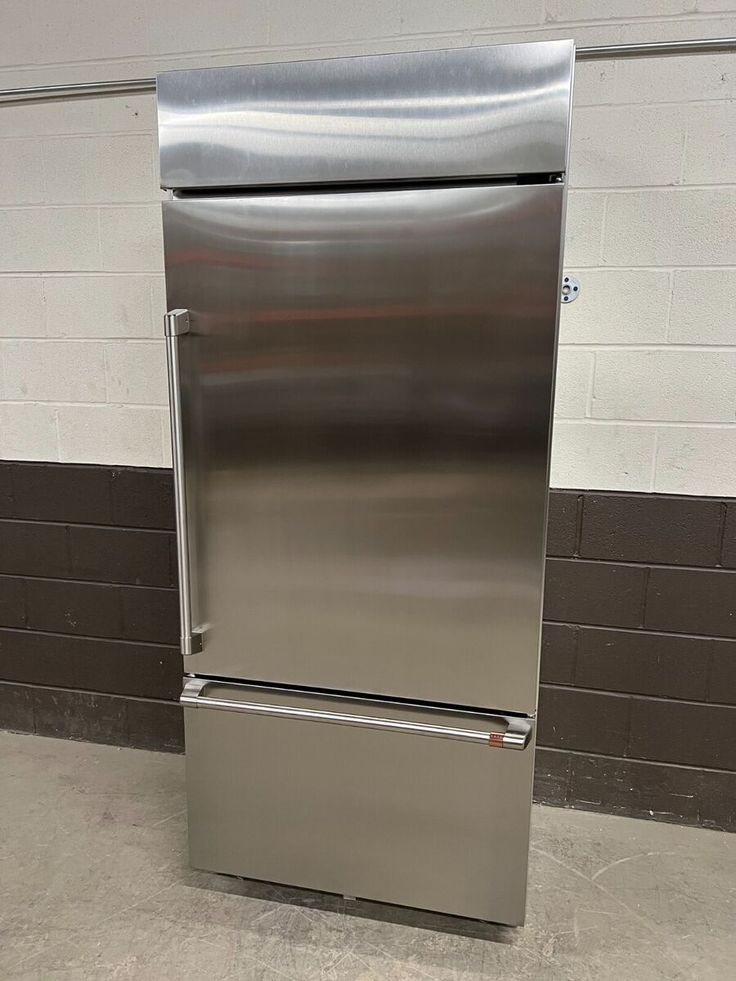 a stainless steel refrigerator sitting in a room next to a brick wall and tiled floor