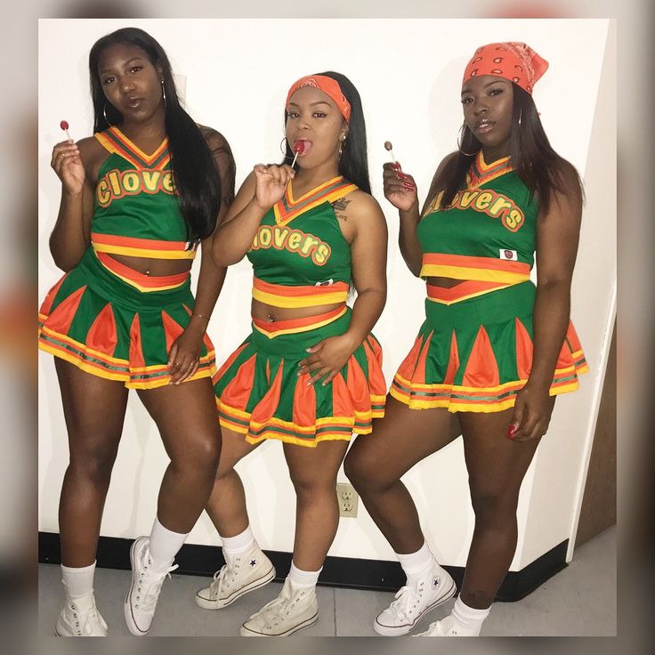 three women dressed in green and orange cheerleader outfits posing for the camera with their tongue out