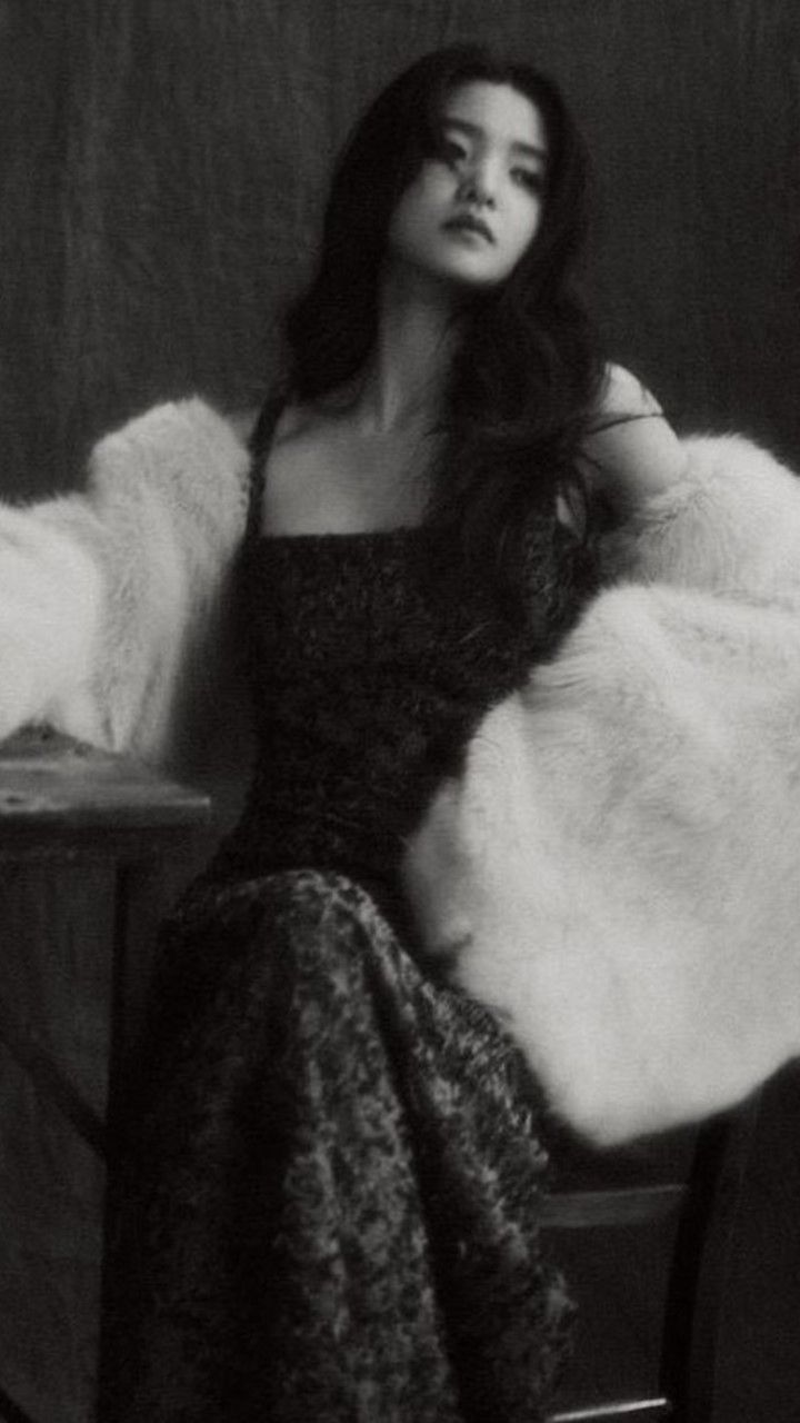 black and white photograph of woman sitting in chair with fur coat over her shoulders, looking to the side