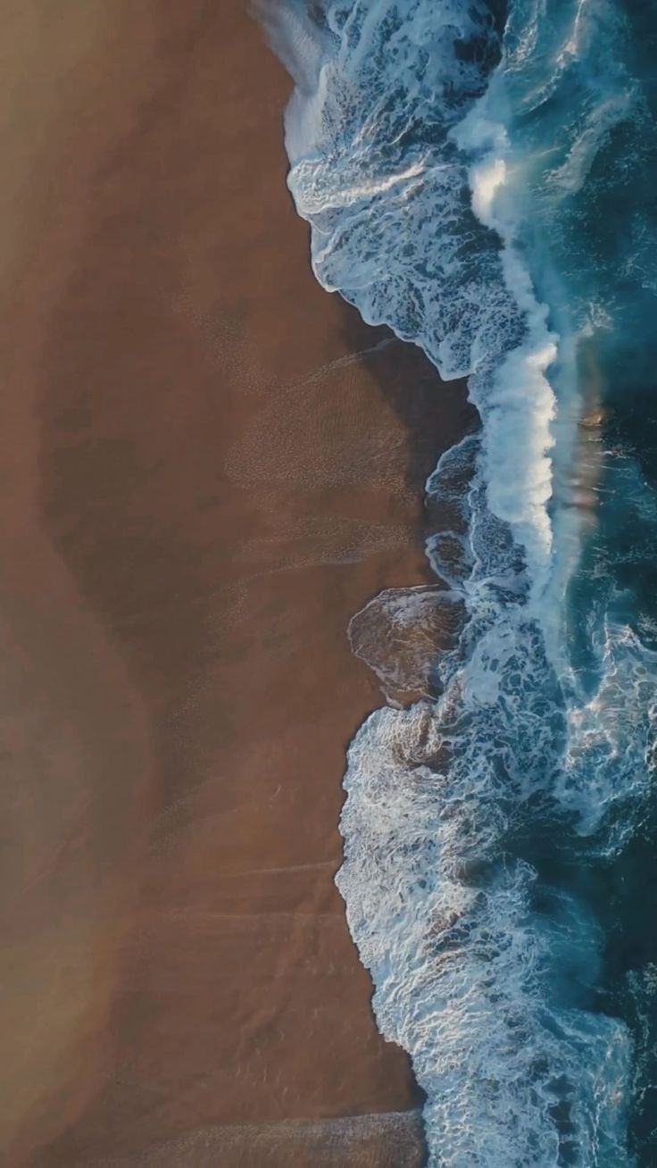 an aerial view of the ocean with waves coming in and people walking on the beach