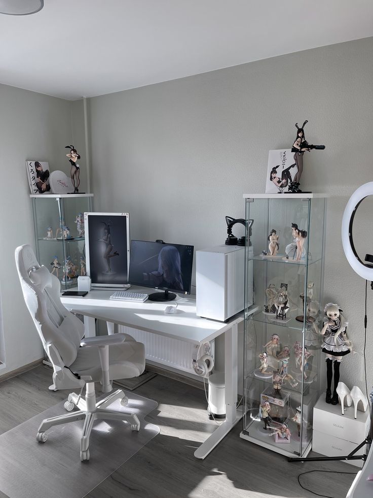 a white desk topped with two computer monitors next to a glass case filled with figurines