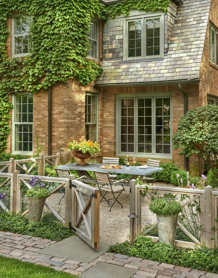 an outdoor patio with table, chairs and potted plants next to a brick house