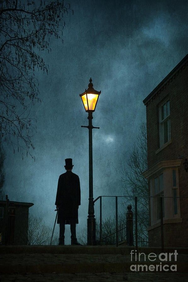 a man standing in front of a street light under a dark sky with the moon behind him