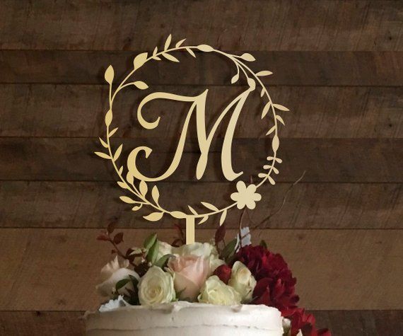 a wedding cake with flowers and a monogrammed topper on a wooden table