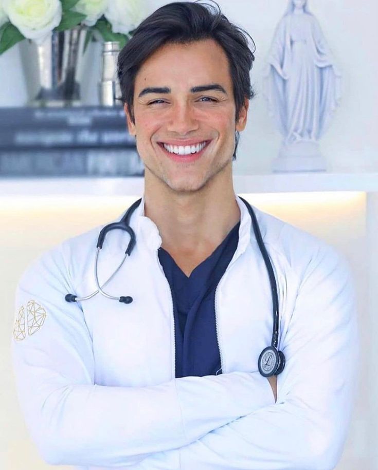 a smiling male doctor standing with his arms crossed in front of a statue and flowers