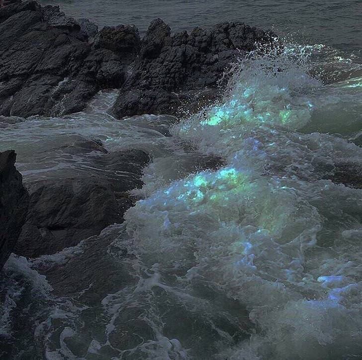 the waves are crashing against the rocks on the beach at night, with green light coming from them