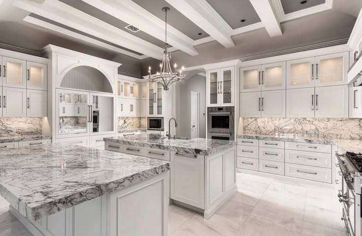 a large kitchen with marble counter tops and white cabinets, along with chandelier